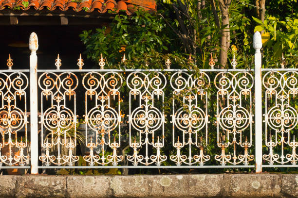 Cast iron white boundary close-up. Retro style cast iron boundary on stone wall, close-up view. Galicia, Spain. Bushes in the background, garden. rusty fence stock pictures, royalty-free photos & images