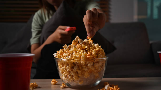 istock Young lady with remote control eating popcorn and watching movie at night. Leisure activity, relaxation, hobby concept. 1417547294