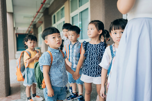 Preschool teacher guiding and arranging students waiting in line entering classroom