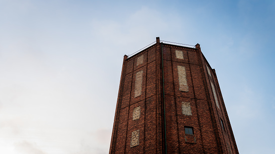 A brick water tower with bricked up windows against a blue sky. Chorzów, Poland