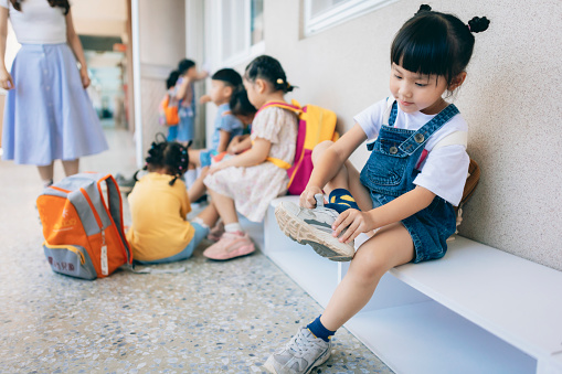 Preschool teacher guiding and arranging students waiting in line entering classroom