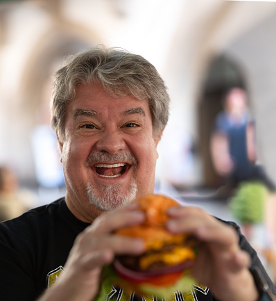 Portrait of man eating a double burger out side. He is very happy