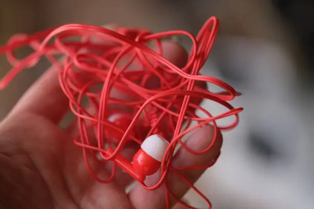 Tangled red headphones in hand. Person trying to unravel broken headphones concept