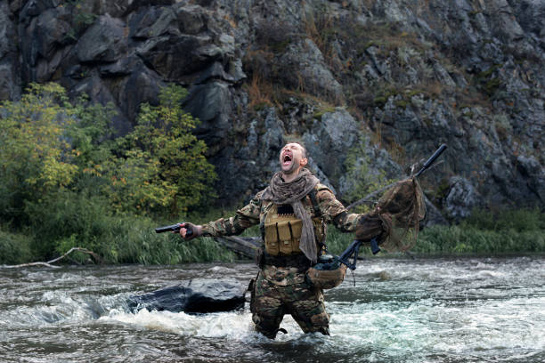 istock Lone mercenary soldier stands knee-deep in river and screaming, arms outstretched with weapons - he lost all his friends. Despair and helplessness. 1417558204