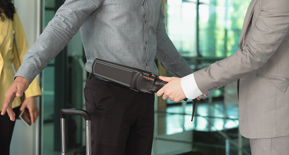 Security officer using a metal detector on a male passenger at airport boarding gate