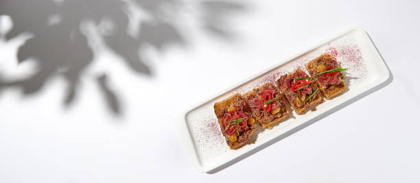 istock Aesthetic composition with shredded beef bruschetta on white background with shadows from flowers. Italian bruschetta with shredded beef and mustard on fine dining in summer. Elegant menu concept. 1417559833