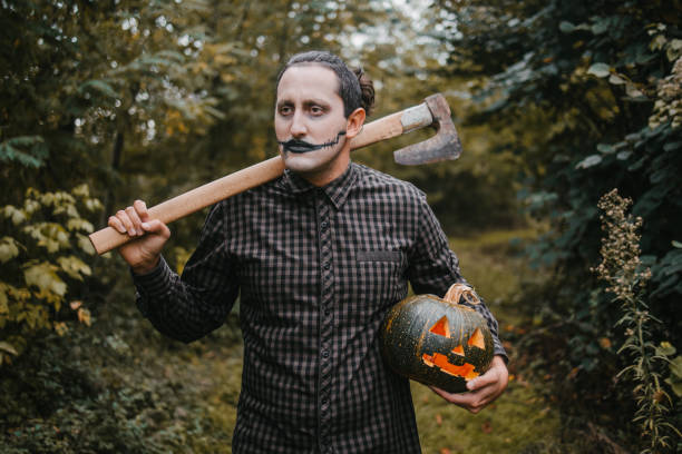 Scary man with an axe holding a lighting pumpkin in forest
