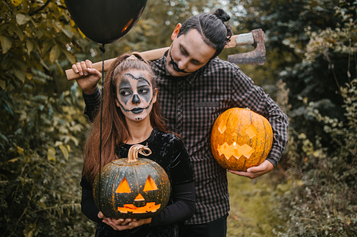 Man and a woman in Halloween costumes holding two carved pumpkins, axe and balloons. Halloween monsters