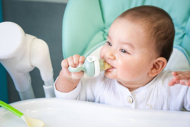 istock A happy and contented baby eats banana puree from a nipple. Introduction of complementary foods, healthy baby food, feeding the baby at the table 1417560995
