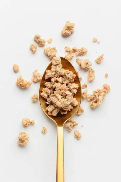 Granola on spoon on light background. Homemade breakfast on white table. Top view of healthy food.