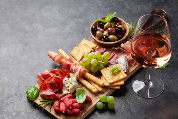 Antipasto board with prosciutto, salami, crackers, cheese, olives Antipasto board with prosciutto, salami, crackers, cheese, nuts, olives and rose wine. With copy space appetizer plate stock pictures, royalty-free photos & images