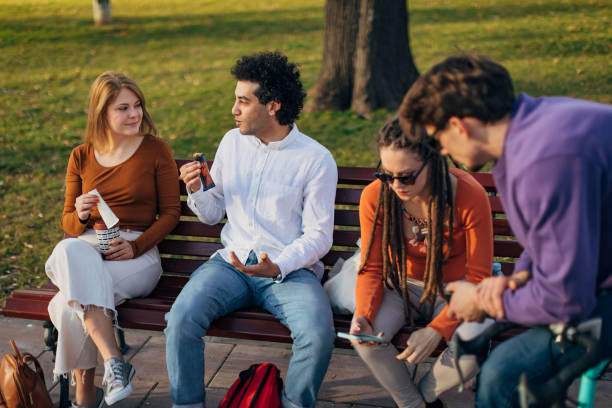 istock Four young people are sitting on a park bench and hanging out 1417565016