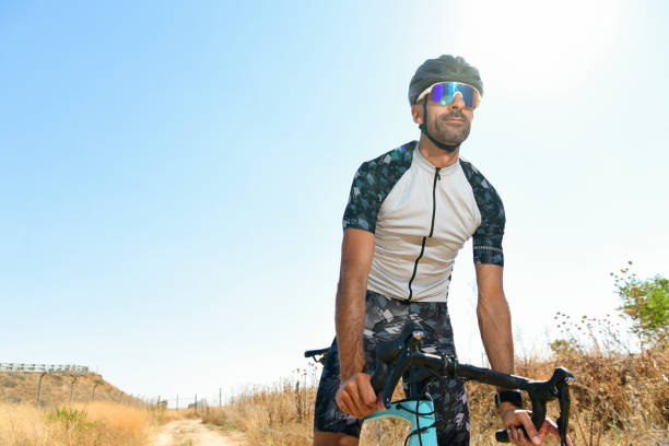 cyclist pedaling his racing bike outdoors with all his safety equipment: helmet, sunglasses, on a sunny day - playing field effort outdoors human age imagens e fotografias de stock