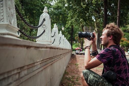 A closeup of a man with a camera taking a photo of unique sculptures with chains outdoors