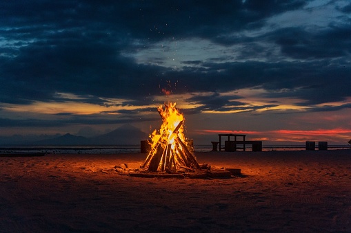 A scenic view of a bonfire on a sandy beach against a vibrant sky at night