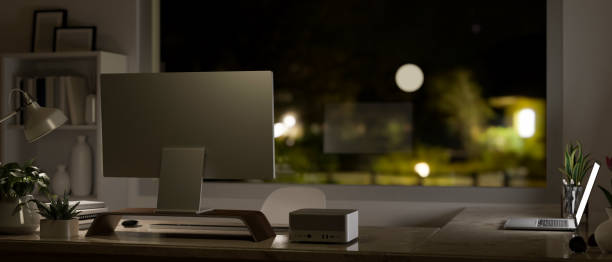 Modern office desk in the darkness room at night with pc computer, laptop on the table. back view
