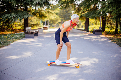 Active senior woman enjoying her free time while skateboarding in park wearing sports clothes and headphones