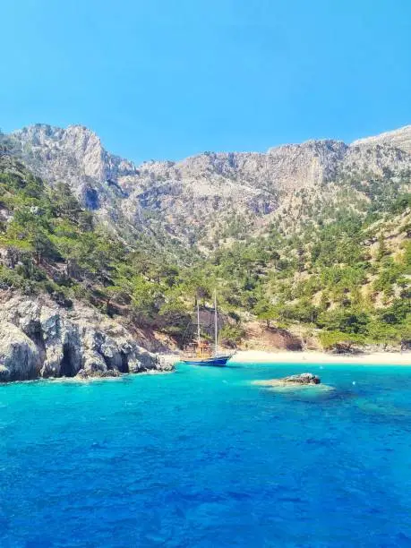 blue sailboat in front of mountains on apella beach in Karpathos, Greece