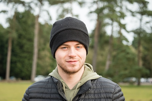 A closeup shot of an attractive aucasian male wearing black winter hat with trees in the background
