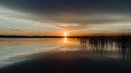 Sunset reflecting in the water with reeds and the horizon in the distance over Candle Lake in Northern Saskatchewan, Canada