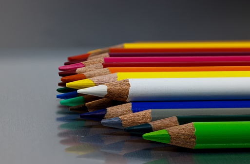 Wooden artists rainbow of drawing pencil crayons are laying in a straight diagonal line on a white marble background with copy space above them.