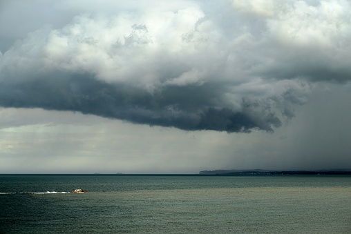 A big gloomy cloud over the wavy sea and a yacht in the waters