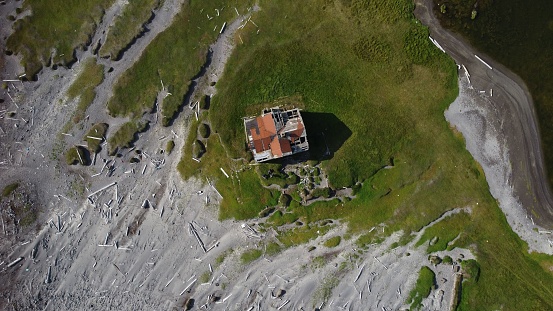 An aerial shot of a ruined hut on a coastline with green grass and white sand