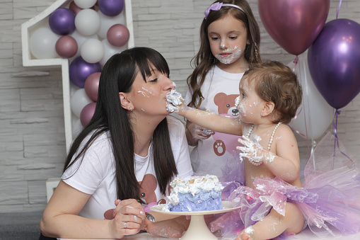 Pretty young woman with her daughters at birthday table they are eating cake