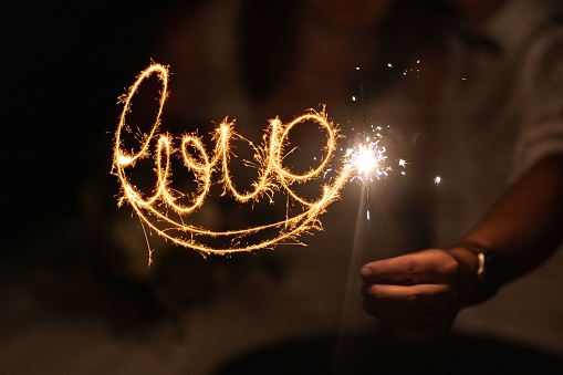 A closeup shot of a wedding celebrated with 'love' sparklers in hands at night