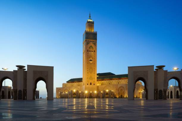 moschea di hassan ii illuminata con il suo riflesso sul terreno lastricato di casablanca, marocco - moschea hassan ii foto e immagini stock