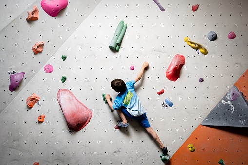 A boy hanging on climbing wall inside on colored hooks