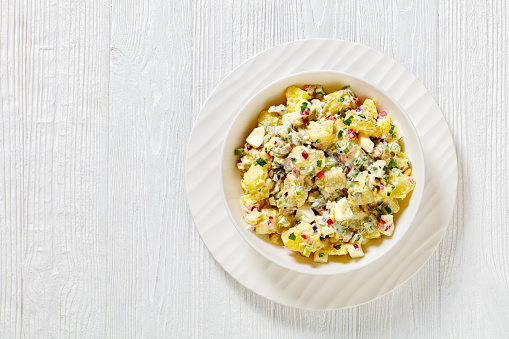 shout hallelujah potato salad with pickles, celery, eggs, jalapeno and mayonnaise dressing in white bowl on wooden table, american cuisine, horizontal view from above