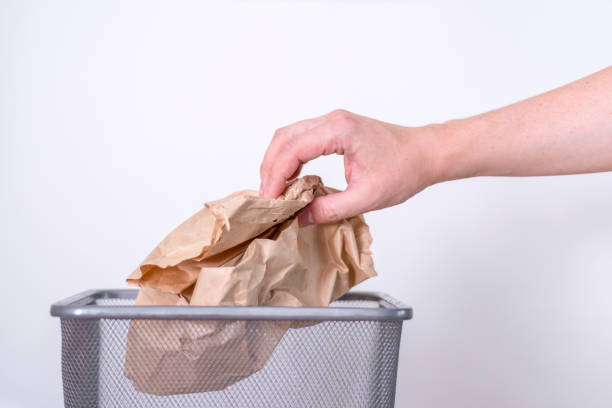 istock A hand throws a crumpled paper bag into a trash can. 1417601570