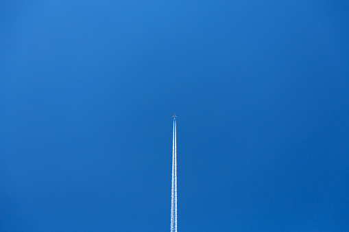 An overhead view of an airplane flying across a blue sky, leaving a white contrail behind it.