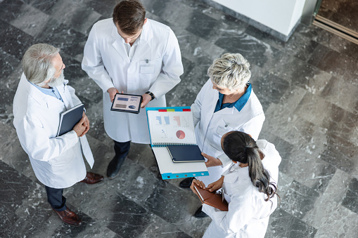 Top-down photo of a diverse group of doctors standing in a corridor, communicating and analyzing their medical results.