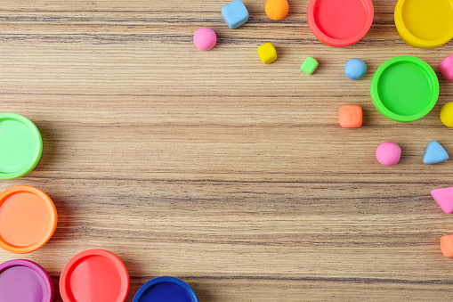 Different color play dough with plastic containers on wooden table, flat lay. Space for text