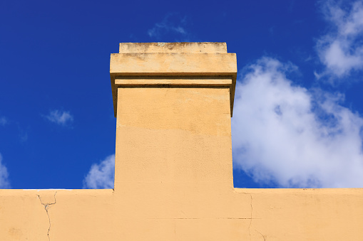 Close-up on a side wall of a building with chimney and deep blue sky beyond.