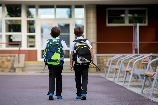 Rear view of school children walking over park after school