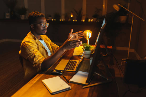 istock Smiling man talking, using online video call in dark office stay overtime to communicate with coworkers 1417612219