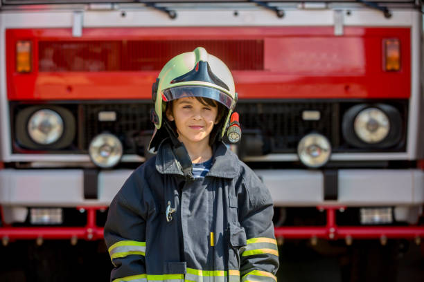 istock Child, cute boy, dressed in fire fighers cloths in a fire station with fire truck 1417612571