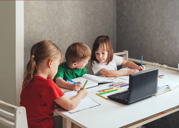 istock Children sit at a table with pens and notebooks and use a laptop 1417614541