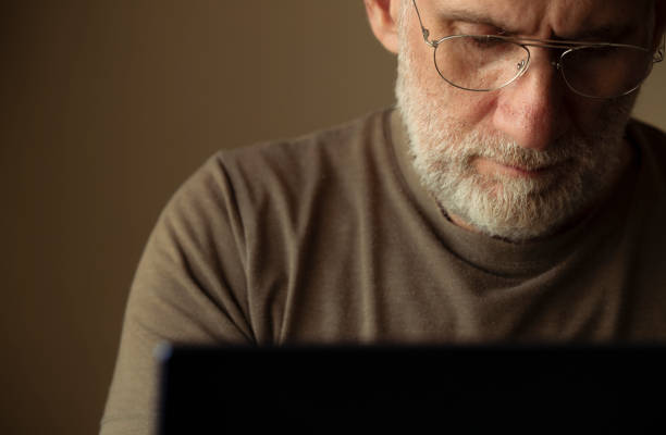 retrato de un hombre adulto con gafas usando una computadora portátil en la habitación - senior men businessman portrait dark fotografías e imágenes de stock