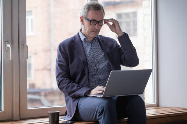 istock Mature man using laptop indoor. Smiling middle aged businessman in glasses 1417619962