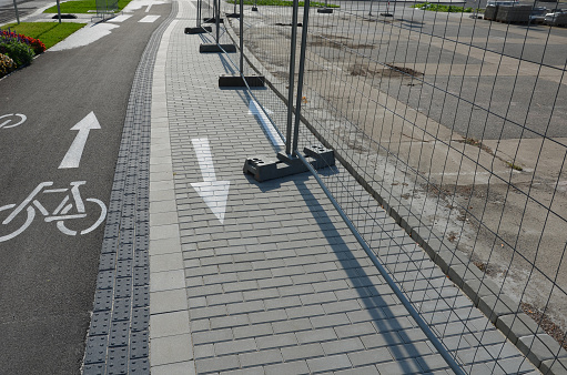 Construction sites with portable fence parts that are installed in plastic weight racks hold the stability of the fencing. along the sidewalk made of interlocking paving