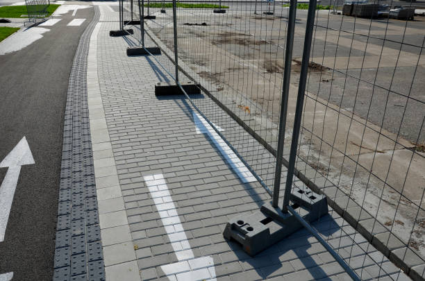 place budowy z przenośnymi częściami ogrodzeniowymi, które są zainstalowane w plastikowych stojakach wagowych, utrzymują stabilność ogrodzenia. wzdłuż chodnika z zazębiającą się nawierzchnią - arrow sign road sign fence zdjęcia i obrazy z banku zdjęć