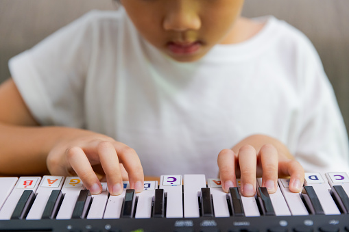 Beautiful little kid boy playing piano in living room or music school. Preschool child having fun with learning to play music instrument. Education, skills concept.
