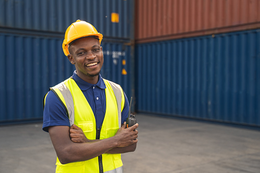 Happy African worker smailing, standing in the container workplace and crossed arms with feeling happiness