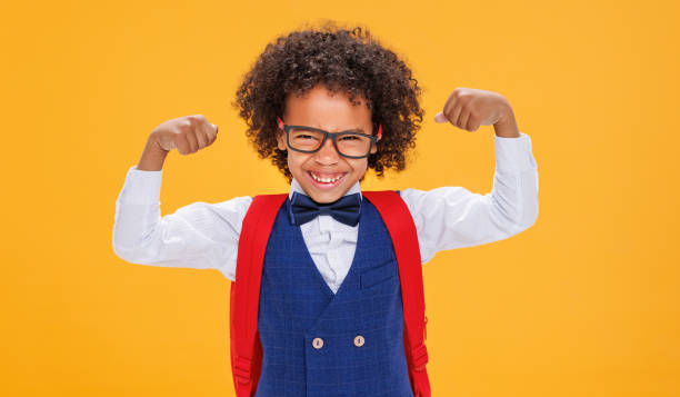 istock Funny curly schoolboy shows strong muscles on color yellow background 1417627193