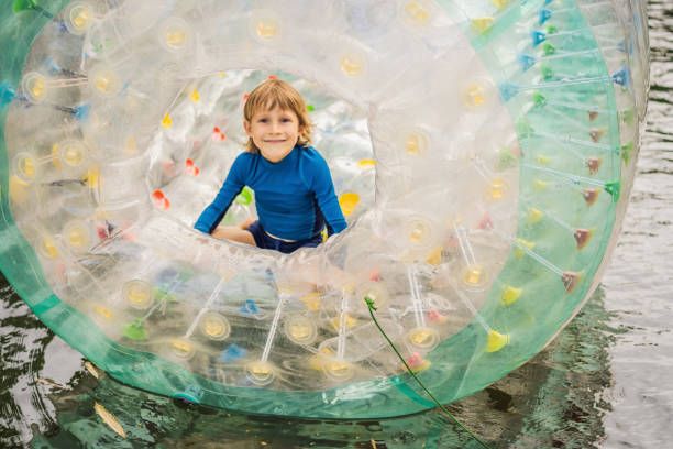 かわいい男の子、ゾーブで湖の真ん中に穴が開いたローリングプラスチックシリンダーリングで遊んでいる - child balloon outdoors little boys ストックフォトと画像