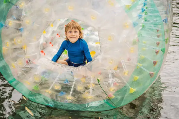 Photo of Cute little boy, playing in Zorb a rolling plastic cylinder ring with a hole in the middle on the lake